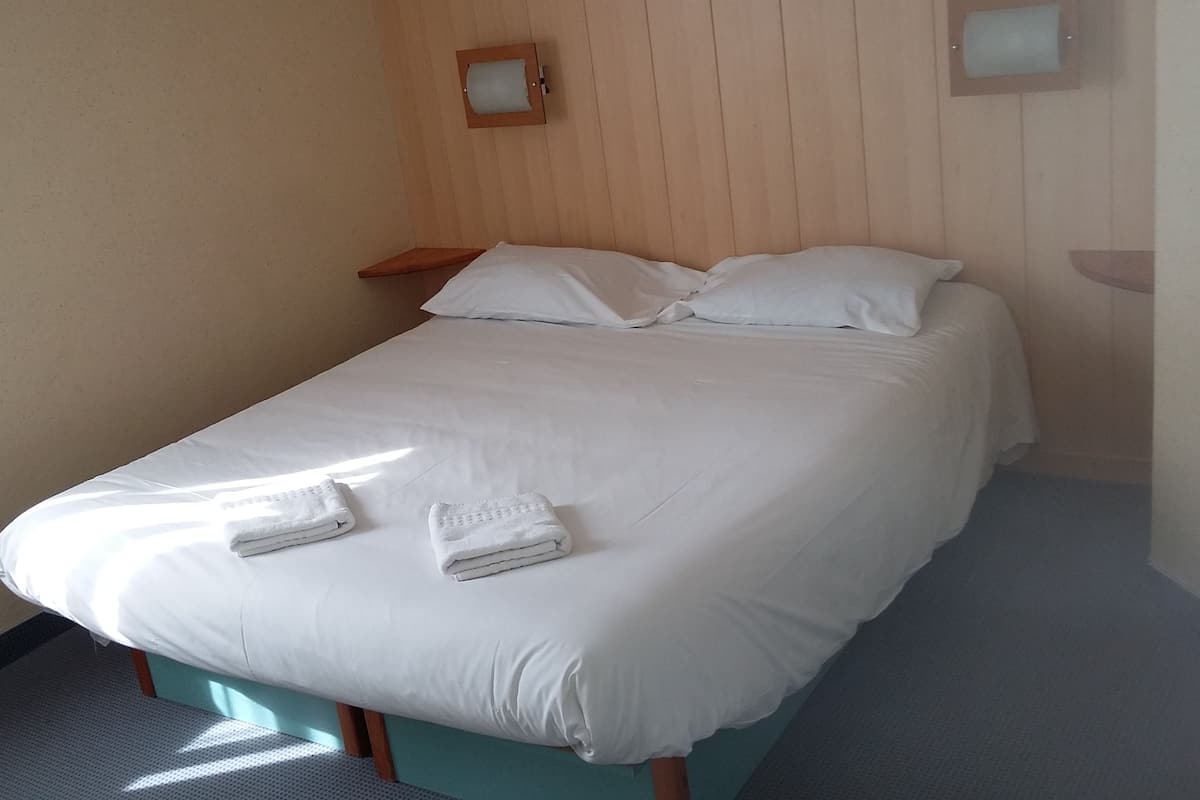 A single bed with white linens and two folded towels, wooden headboard, and a small bedside table.