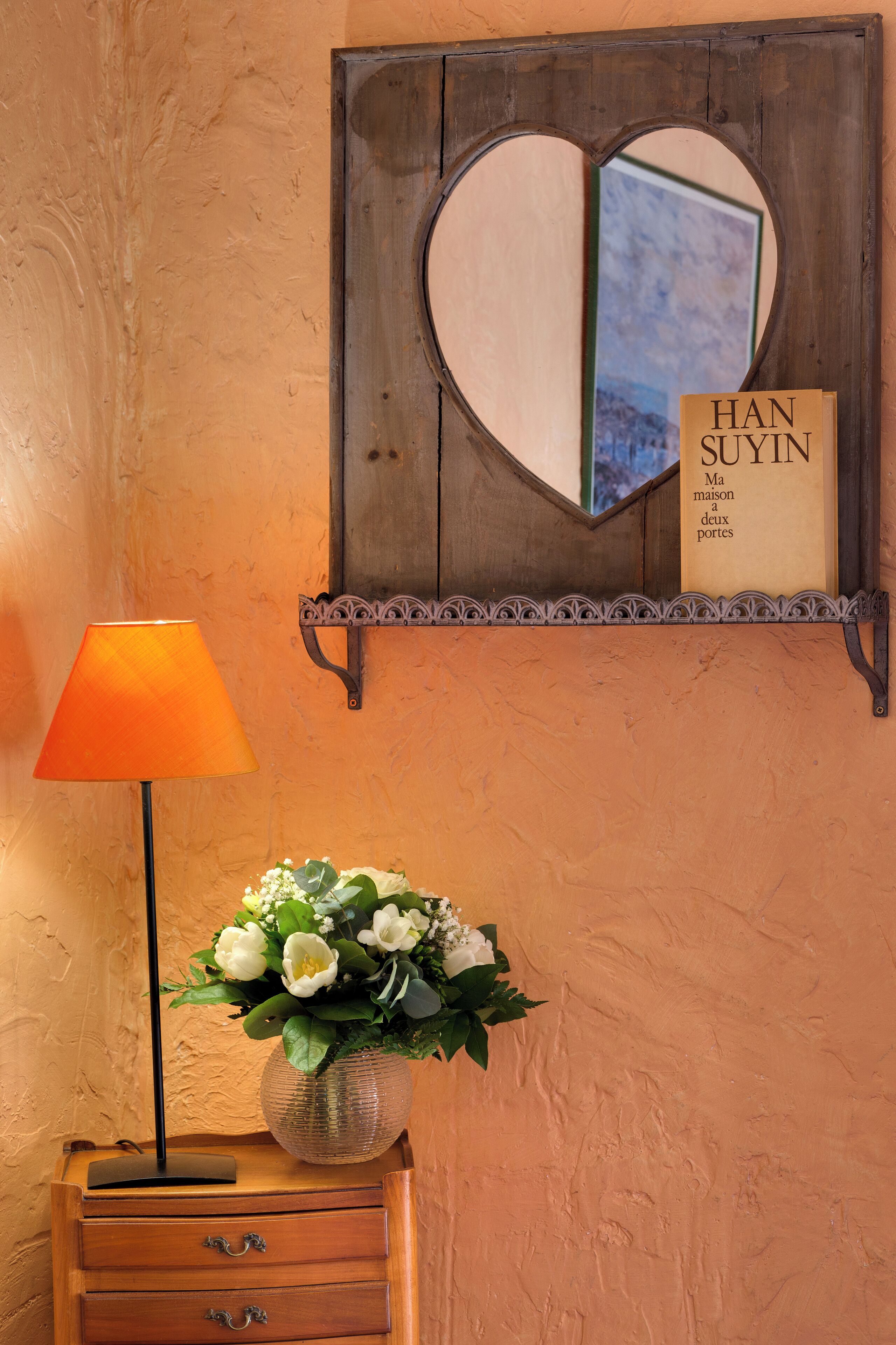 A wooden shelf with a heart-shaped mirror and a book titled 'HAN SUYIN Ma maison a deux portes'.