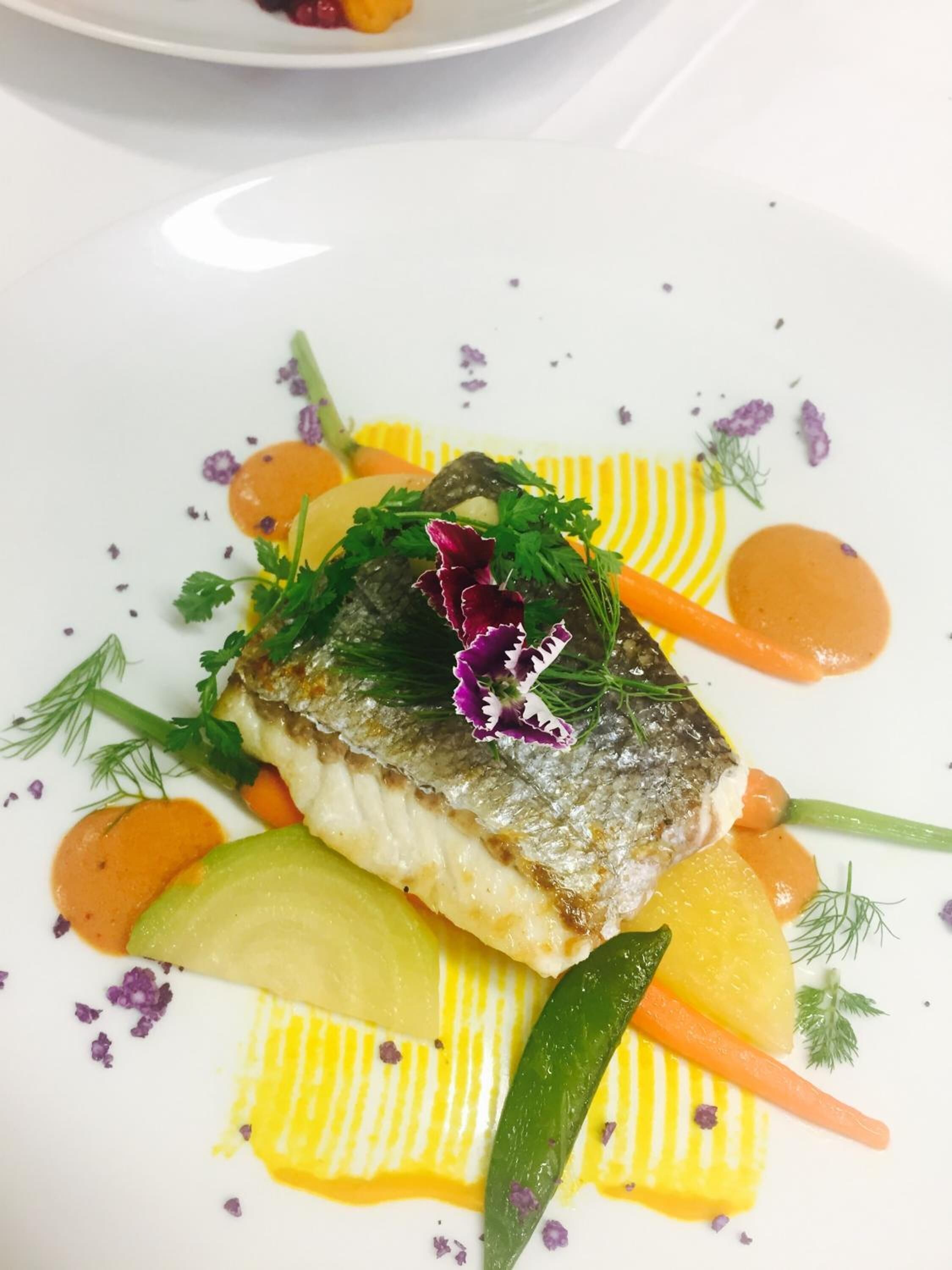 Un plato con pescado, verduras y guarniciones sobre una vajilla blanca.