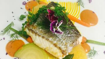 Un plato con pescado, verduras y guarniciones sobre una vajilla blanca.