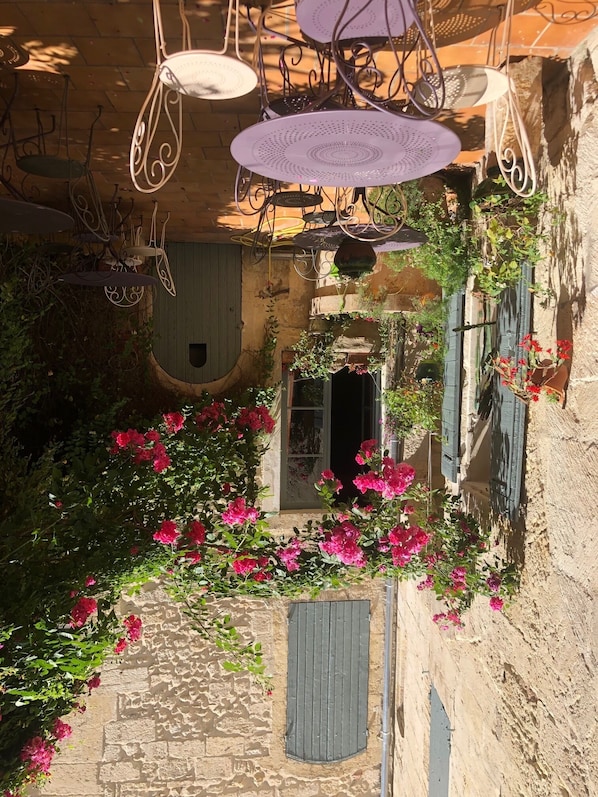 Un patio con sillones colgantes, un muro de piedra y flores rosas en flor.