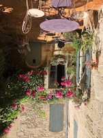 Un patio con sillones colgantes, un muro de piedra y flores rosas en flor.
