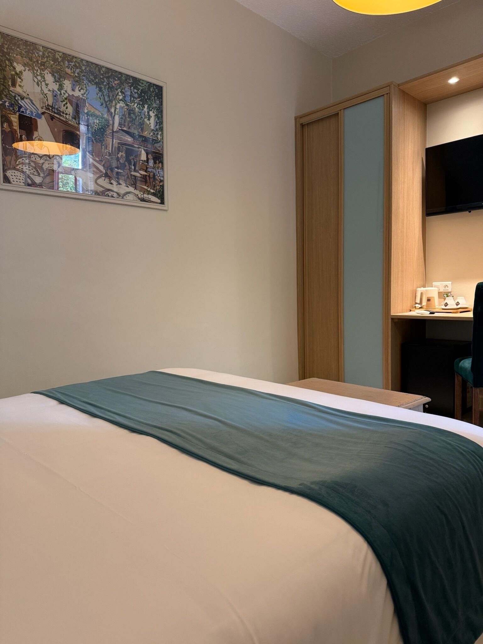 Une chambre d’hôtel avec un lit, un bureau, une chaise, une télévision et un tableau au mur.