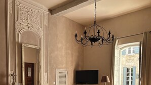 A hotel room with a large bed, two armchairs, a television, and a view of a building through a window. - Du Musée (Arles)