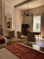 Habitación de hotel con una cama grande, dos sillones, un televisor y vistas a un edificio por la ventana.