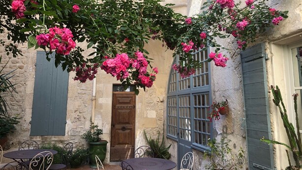 A courtyard with a stone wall, a wooden door, and a window with blue shutters. - Du Musée (Arles)