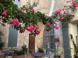 Un patio con muro de piedra, puerta de madera y ventana con contraventanas azules.