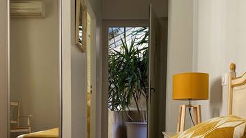 A hotel room with a bed, a bedside lamp, a chair, a potted plant, and an air conditioning unit.