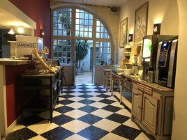 Una cocina de hotel con piso de cuadros, una máquina de café y un refrigerador con la etiqueta 'ANDROS'.
