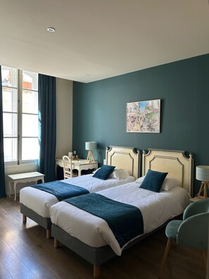 Una cama doble con dos almohadas, una mesita de noche, una silla, un escritorio y una ventana con cortinas.