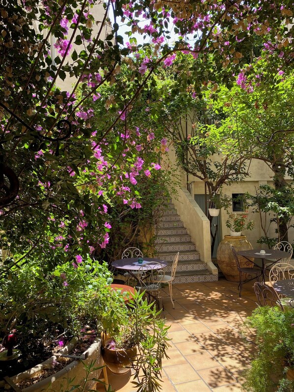 Un patio con una mesa y sillas, rodeado de plantas en macetas y una escalera.