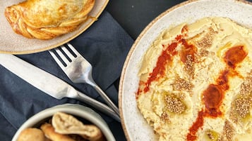 Et bord med mad, herunder skiver af tomat, en skål hummus og kager.