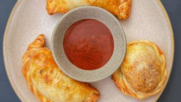A plate with four golden-brown pastries and a small bowl of red sauce.