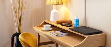 A compact workspace with a wooden desk, a laptop, a lamp, a chair, and a television mounted on the wall.