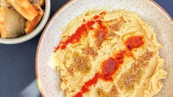 Un tazón de hummus con semillas de sésamo y pimentón, junto a un tazón de pan pita sobre una superficie oscura.