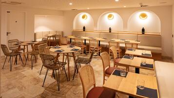 A restaurant with round tables and wicker chairs, a long counter with stools, and a wall with arched windows.