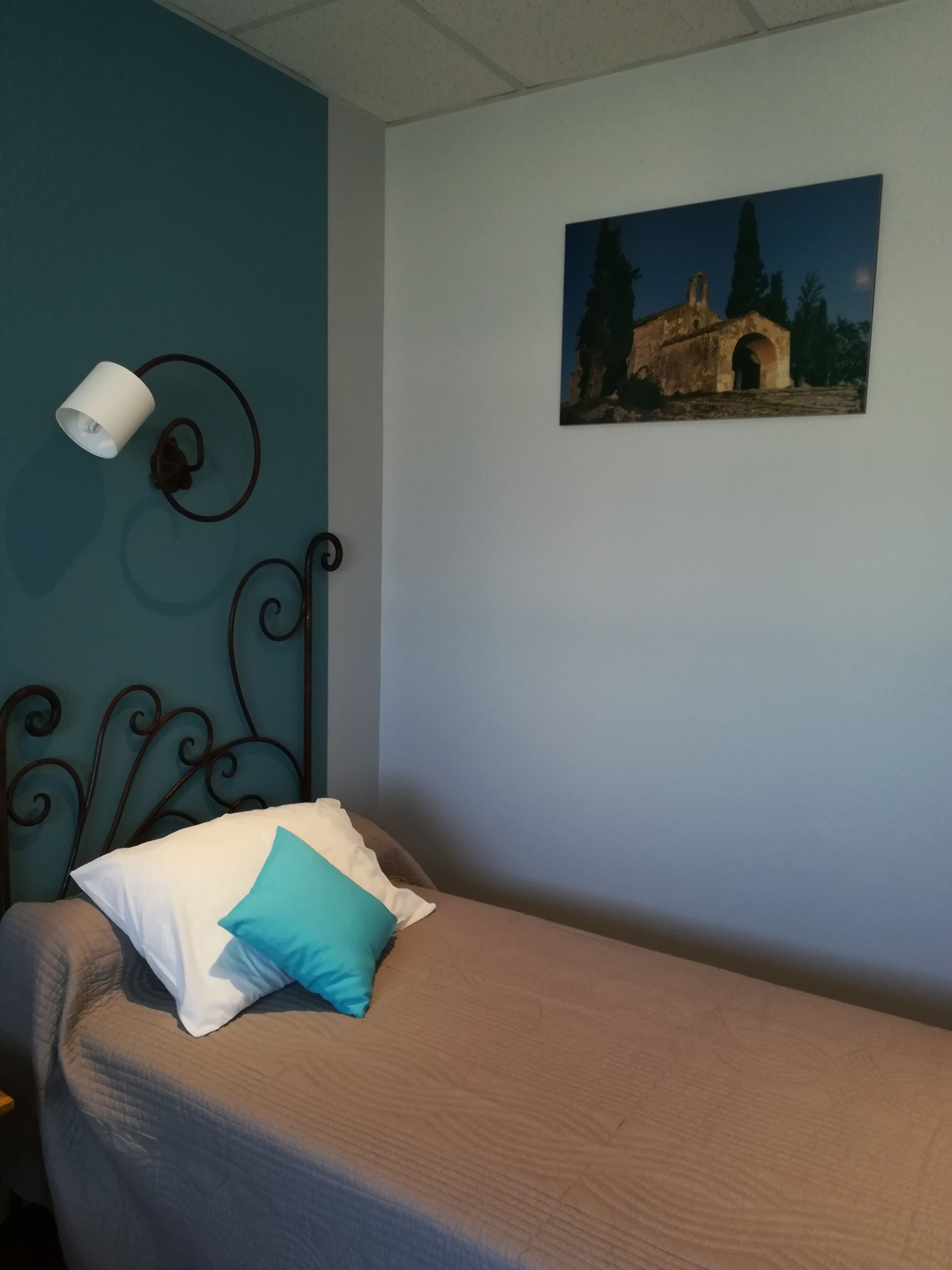 Ein Schlafzimmer mit einem Einzelbett, einer Wandlampe und einem Bilderrahmen mit einem Gebäude darauf.