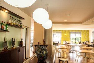 Un restaurante con zona de bar, mesas, sillas y una pared amarilla con diseño.