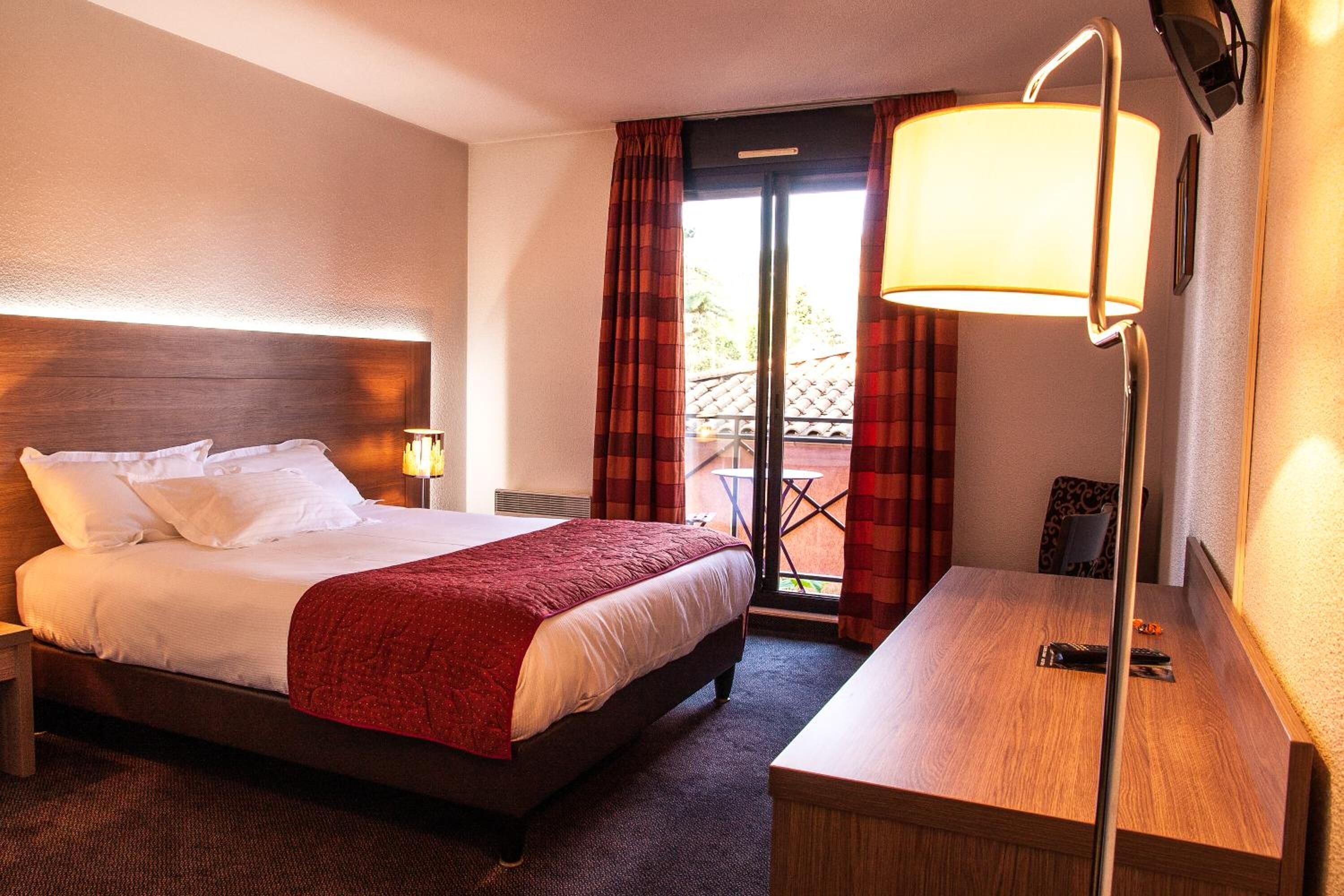 Una habitación de hotel con cama, escritorio, lámpara y vistas al exterior.