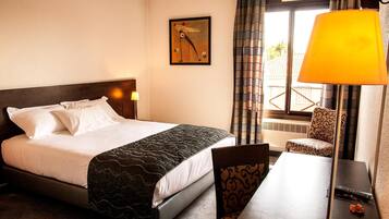 Een hotelkamer met een bed, een bureau, een stoel, een lamp, een raam met gordijnen, en een aan de muur hangend kunstwerk.
