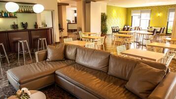 A modern lounge area with a leather sofa, dining tables, and bar stools.
