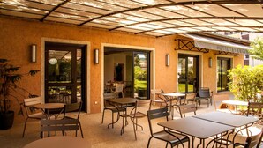 Un espace extérieur aménagé avec des tables et des chaises, un coin salon abrité et une vue sur un jardin.