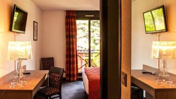 A hotel room with a wooden desk, two lamps, a chair, a bed, and a TV on the wall.