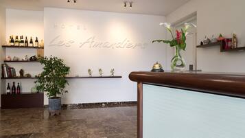 A hotel reception area with a marble floor, a large potted plant, and shelves displaying wine bottles and decorative items.
