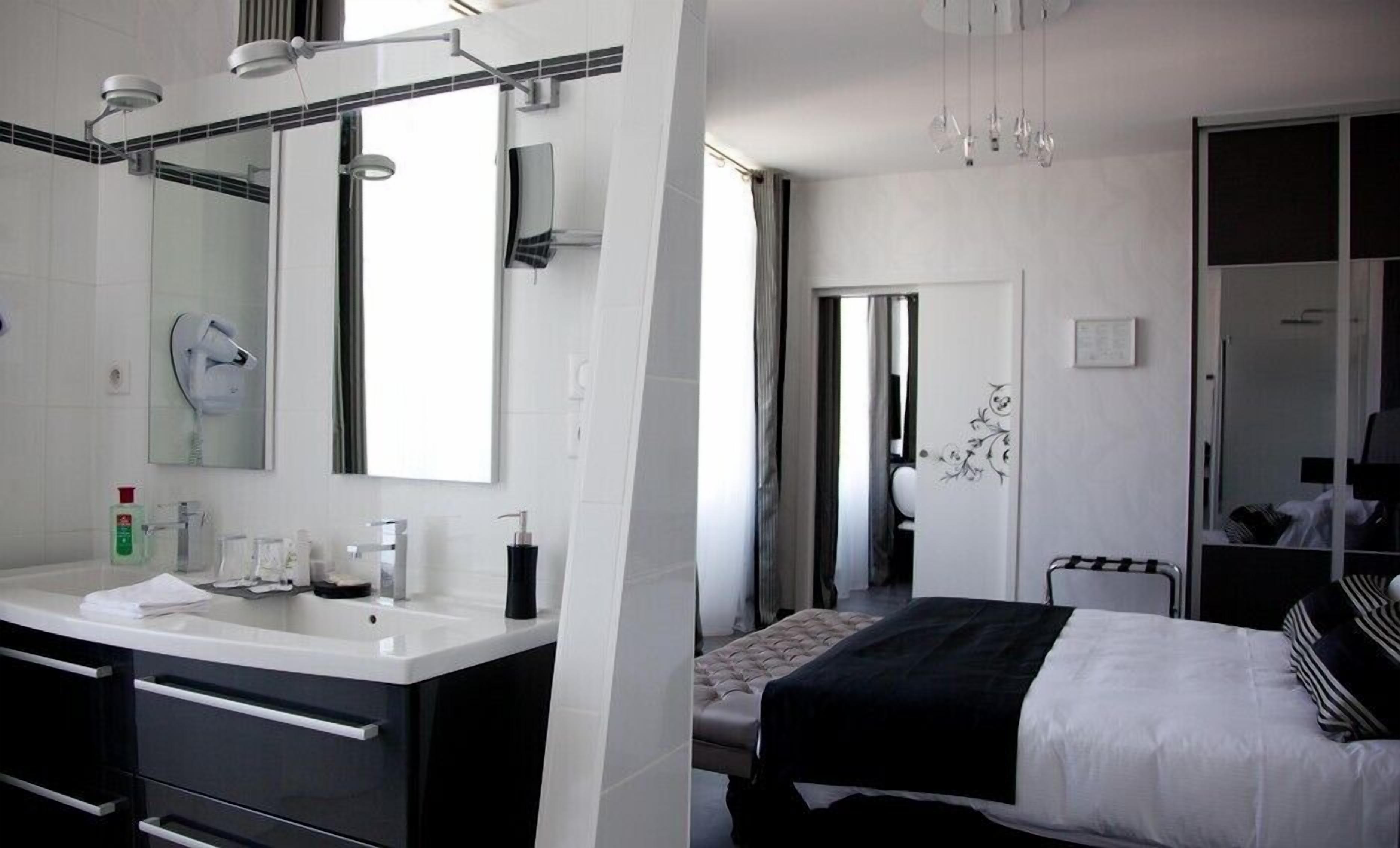 Una habitación de hotel moderna con un espejo grande, un tocador con lavabo y una cama con una colcha a rayas blancas y negras.