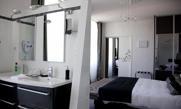 A modern hotel room with a large mirror, a vanity with a sink, and a bed with a black and white striped blanket. - Domaine de Roullet (Roullet-Saint-Estephe)