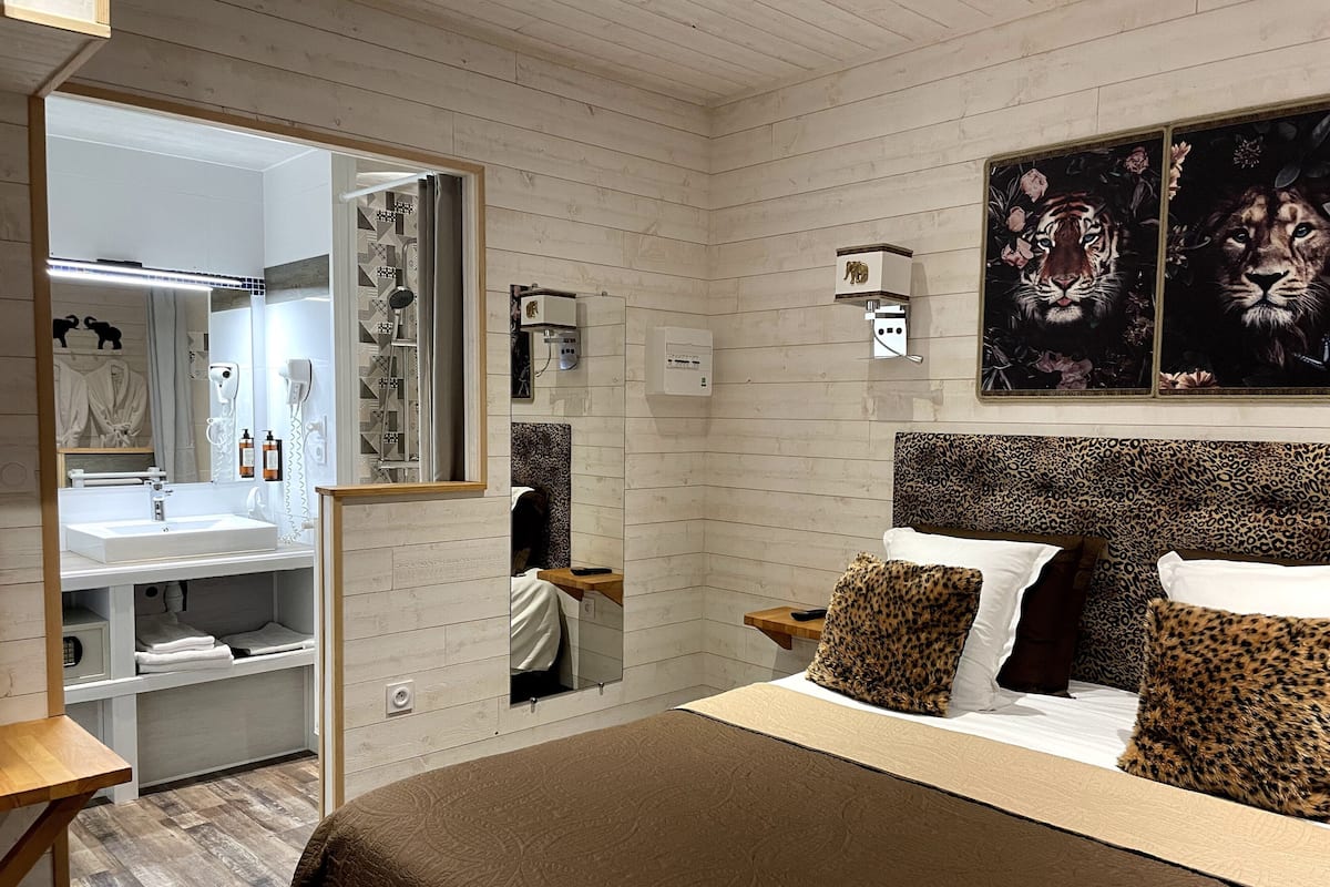 Une chambre moderne avec une tête de lit en bois, un grand miroir, un lavabo blanc et un lit agrémenté d’oreillers à motifs léopard.