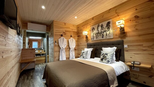 A wooden-paneled bedroom with a bed, two wall-mounted lights, and a painting of horses.