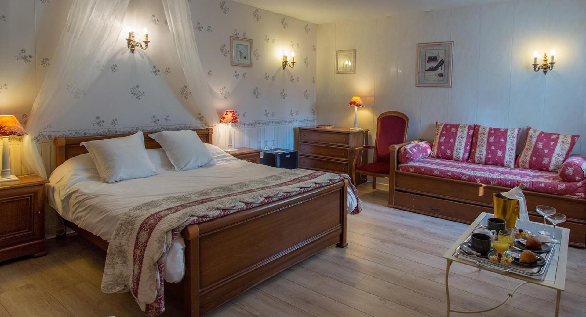 A bedroom with a wooden bed, a red sofa, a nightstand, a dresser, and a bedside table with a lamp.