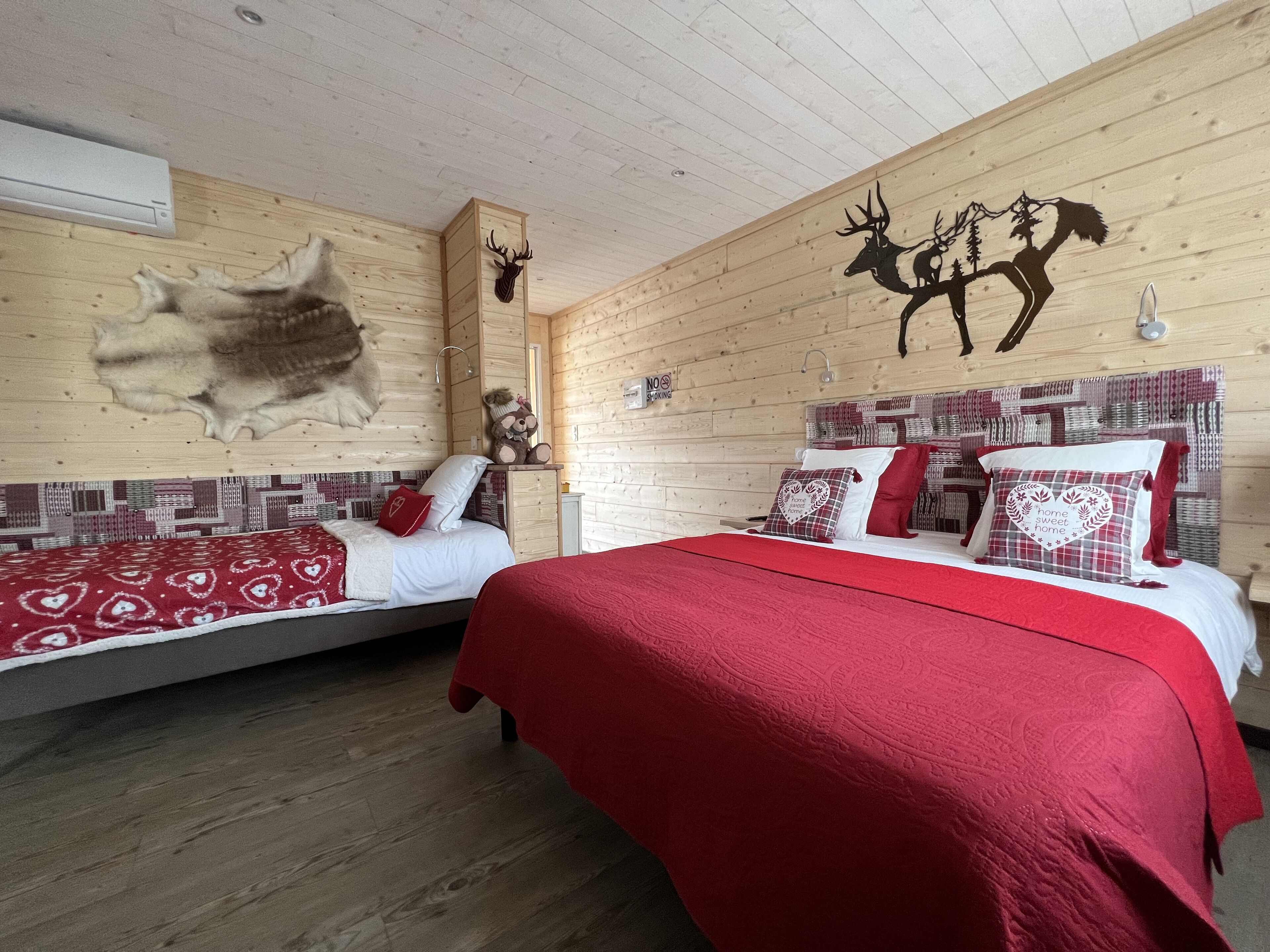 Una habitación acogedora con dos camas, paredes de madera, un trofeo de caza y un cartel de 'No Fumar'.