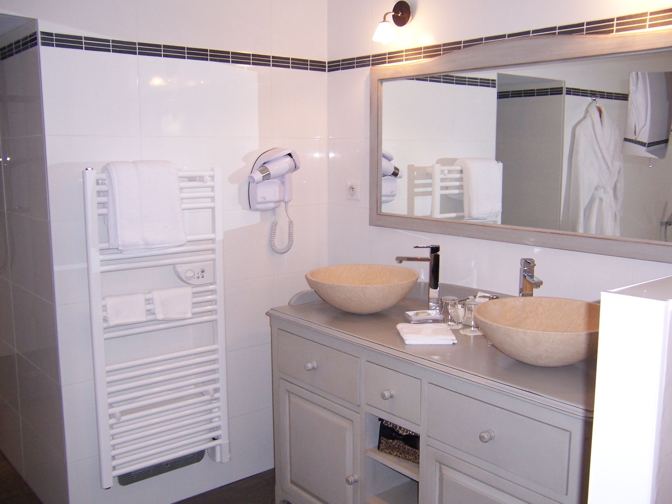 A bathroom with a white vanity, two large bowls, a mirror, and a towel rack.