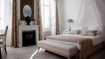 A bedroom with a large bed, a bedside table, a chair, a fireplace, and a window with curtains.