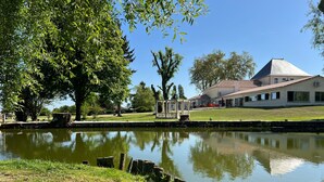 A serene lakeside view with a gazebo, a grassy area, and a building with a sloped roof in the background.