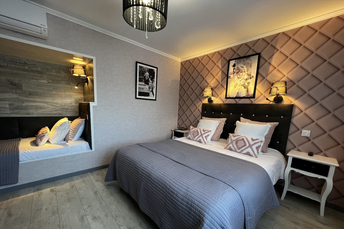 Une chambre moderne avec un grand lit, un banc intégré près de la fenêtre et un panneau décoratif mural.