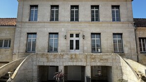 A two-story stone building with a central entrance, large windows, and a tiled roof.