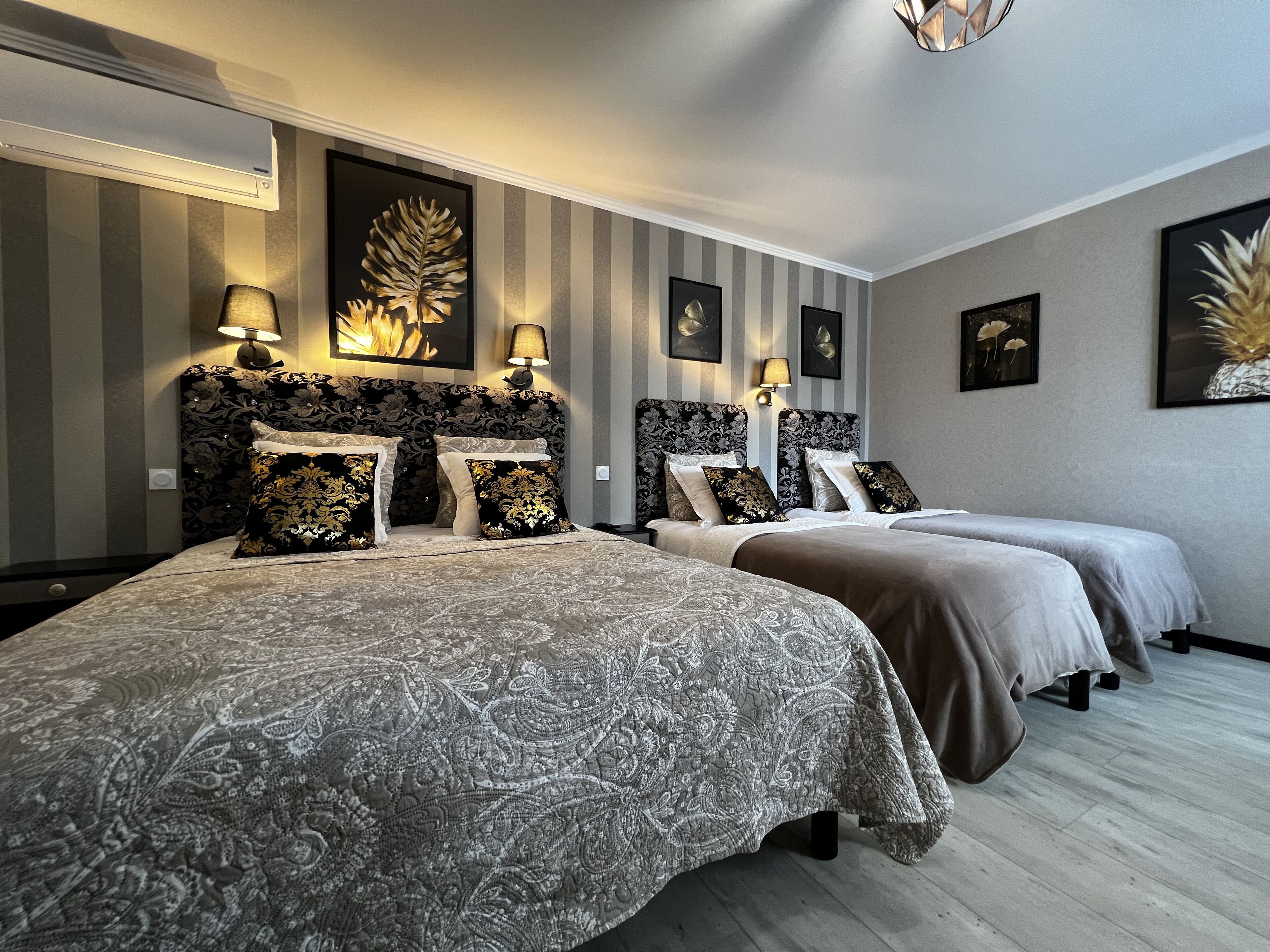 A hotel room with two beds, each with a patterned bedspread and matching pillows. There are wall-mounted lamps and framed artwork on the walls.