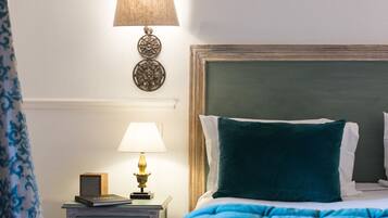 Un lit bien fait, agrémenté d’un coussin turquoise, d’une lampe de chevet et d’une lampe fixée au mur.