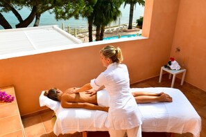 Sesión de terapia de masaje en una camilla blanca, con vista a una piscina y palmeras.