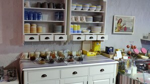 A kitchen with shelves of dishes, jars, and a table with food items. - Logis Hotel Les Bleuets (Royan)