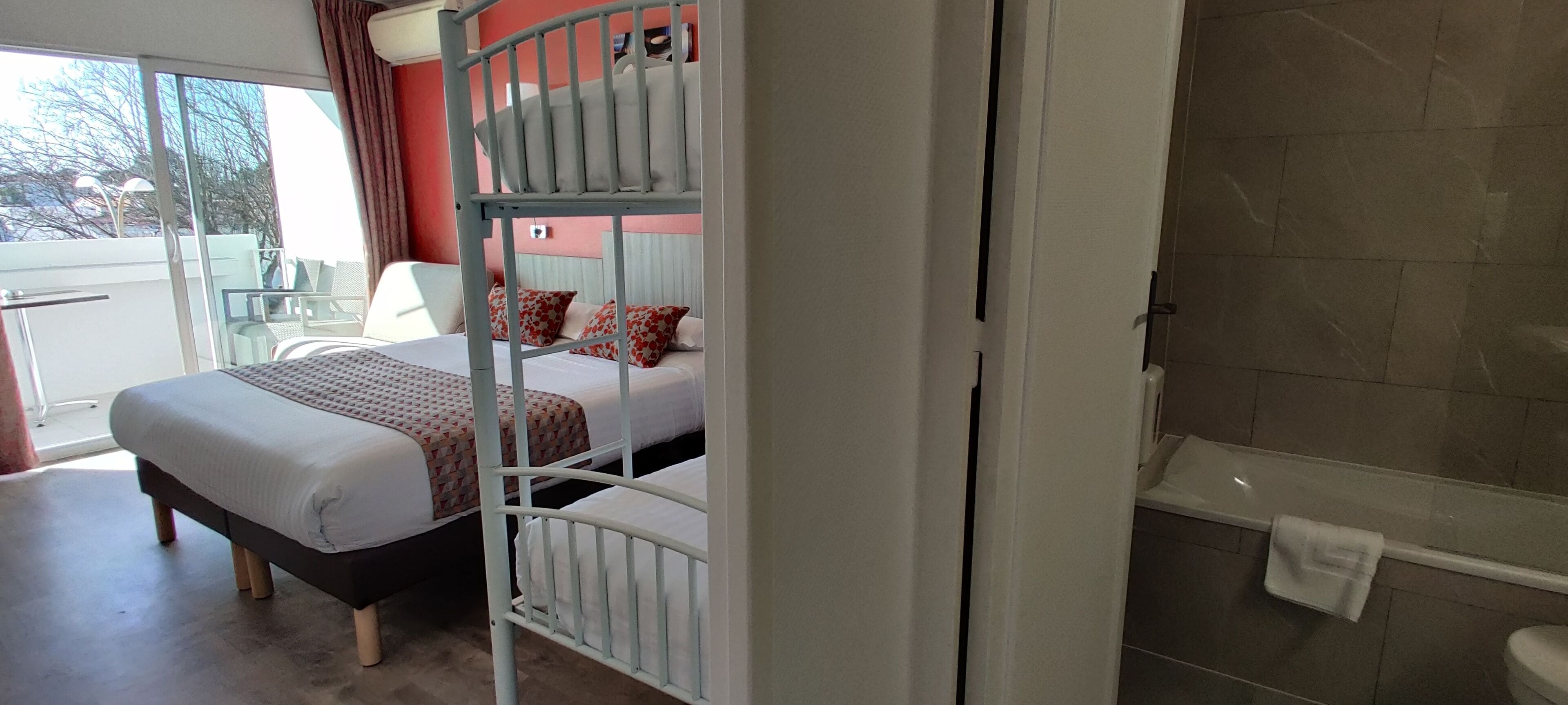 A hotel room with a bunk bed, a bathroom with a bathtub, and a balcony with a chair.