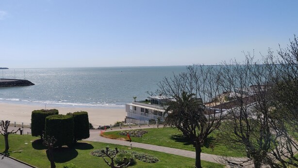 A coastal view with a beach, a promenade, and a modern building with a flat roof. - Logis Hotel Les Bleuets (Royan)
