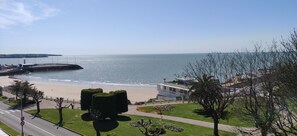 Vista costera con playa, paseo marítimo y un edificio moderno de techo plano.