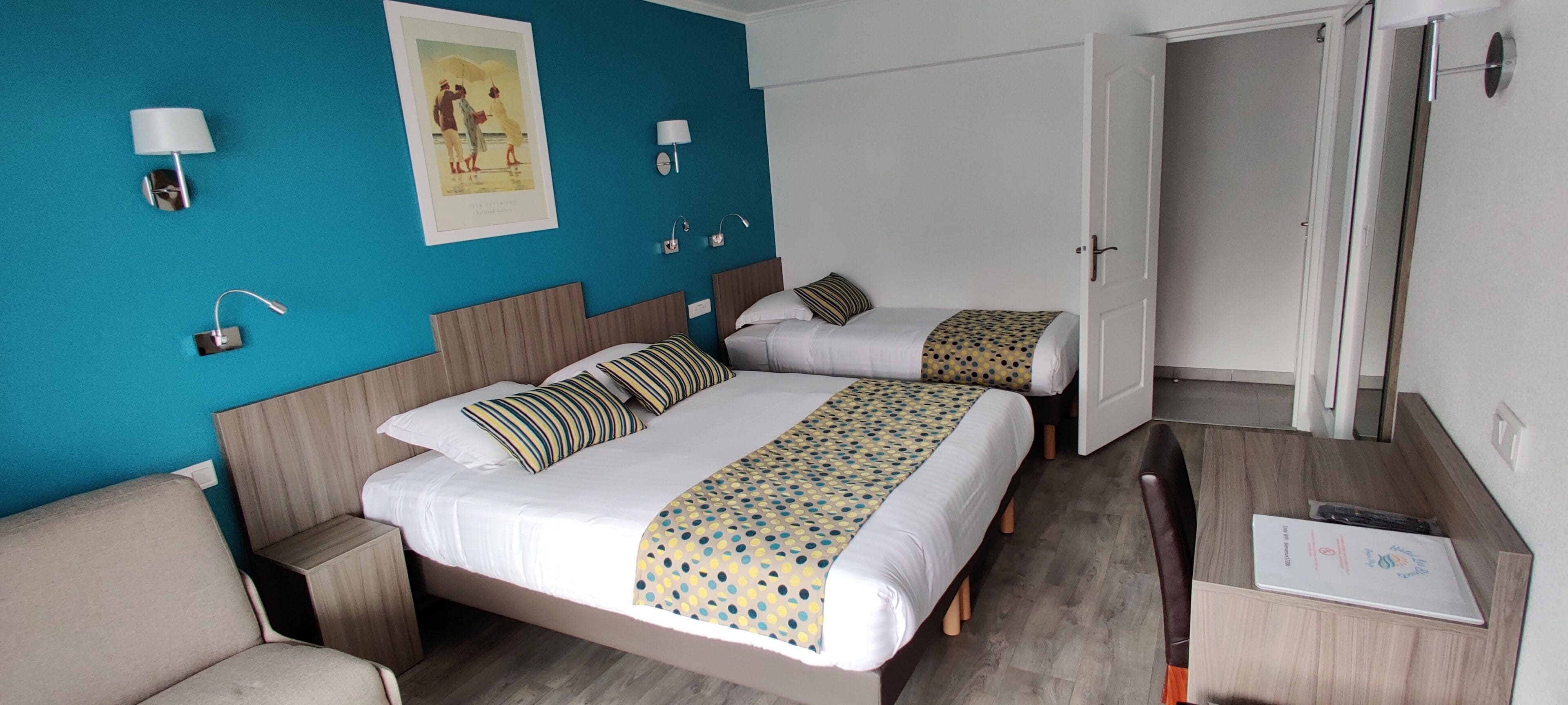 Ett hotellrum med två sängar, ett skrivbord och en stol. Det finns vägglampor och en inramad tavla på väggen.