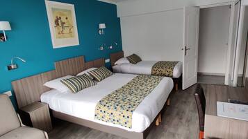 Ett hotellrum med två sängar, ett skrivbord och en stol. Det finns vägglampor och en inramad tavla på väggen.