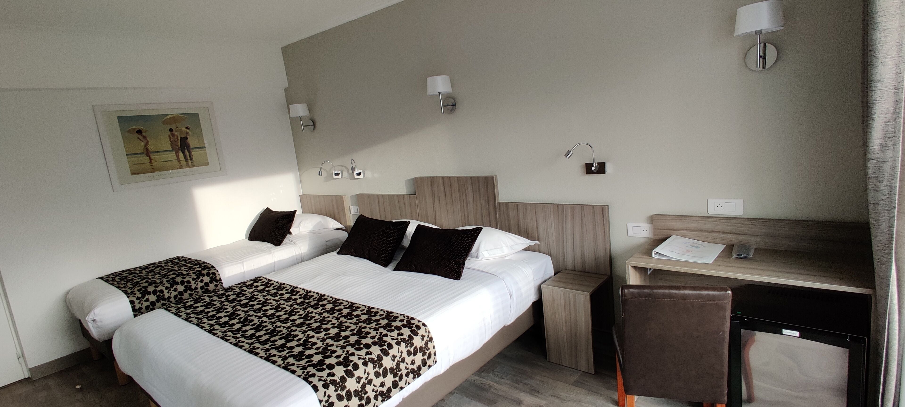 A hotel room with a large bed, two bedside tables, a desk with a chair, and a wall-mounted lamp.