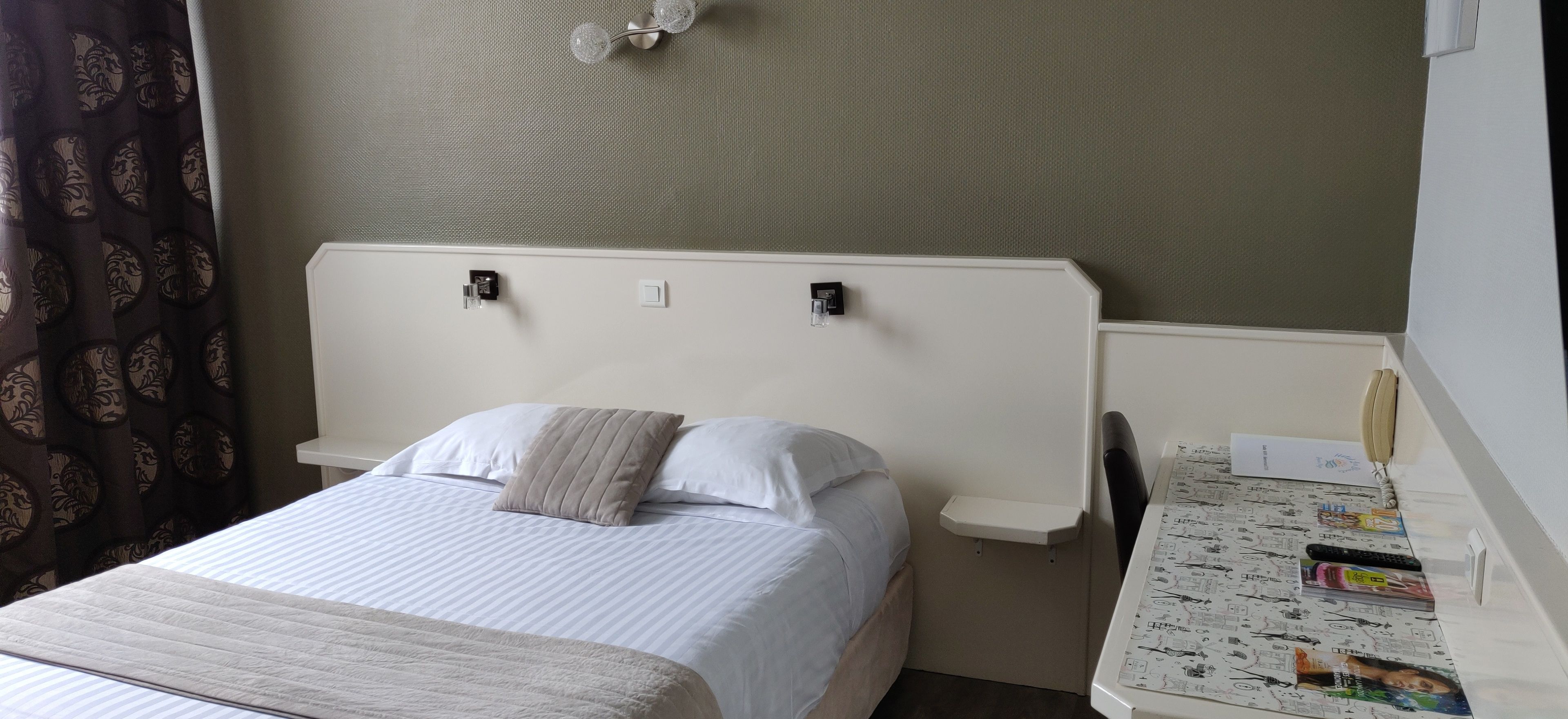 Een hotelkamer met een bed, nachtkastje met een lamp, een stoel en een klein bureau met stoel.